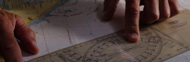 Close-up of the hands of a person preparing a marine route using a map and a ruler
